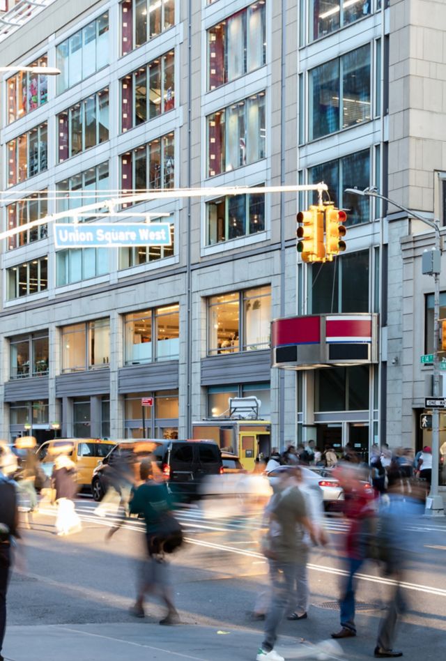 Crowds of people walking across the busy intersection on 14th Street at Union Square Park in New York City NYC past the cars and buildings