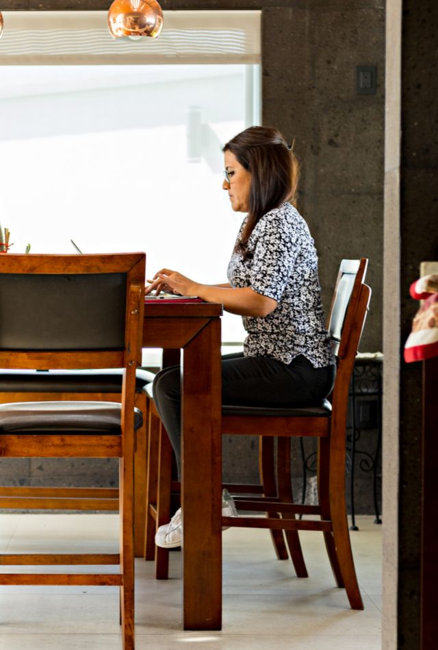Lady woman typing on her computer sitting at her dining room table. Female person carrying out her work activities remotely from her home.