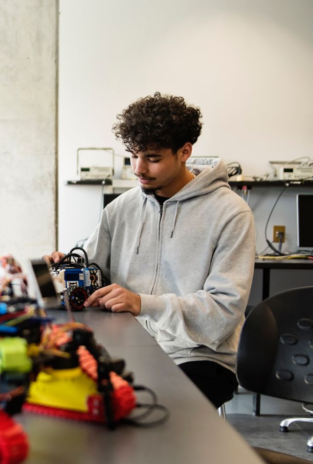 College student in robotics classroom working on an electronic device.