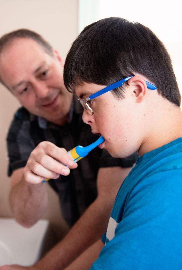 Father helping son with Down Syndrome brush his teeth