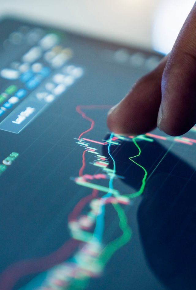 A person's hand interacting with a tablet showing financial stock market graphs and data.