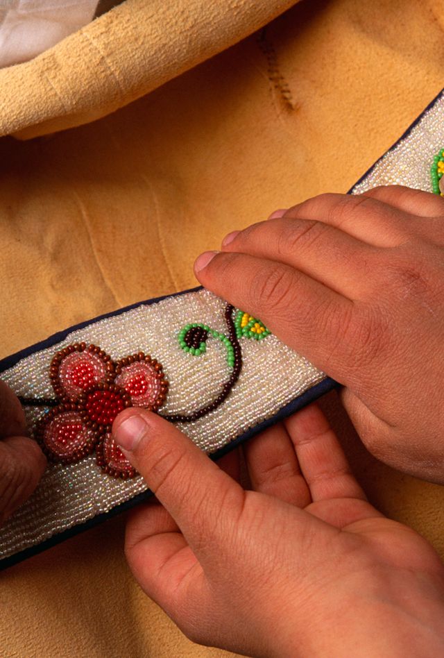 Closeup image of two sets of hands, one of an older person and one of a child holding a beaded cloth