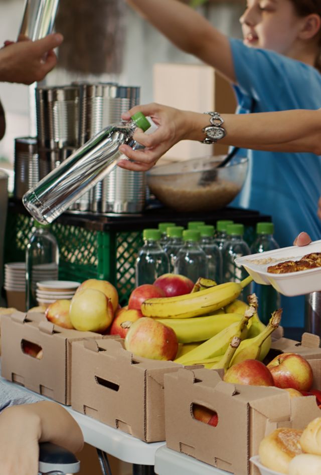 At food drive, poor female wheelchair user receives free food and provisions. Multiethnic volunteers in blue t-shirt distributing fresh fruits and hot meals to less privileged. Close-up, tripod.