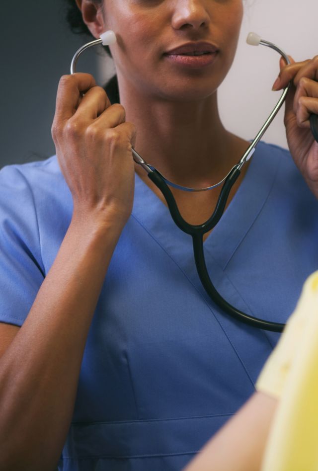 Medical professional holding stethoscope, patient with gown is blurred in foreground.