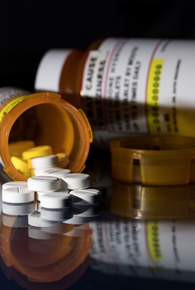 Two bottles of prescription medicine lay on their side on a table with pill spilling out