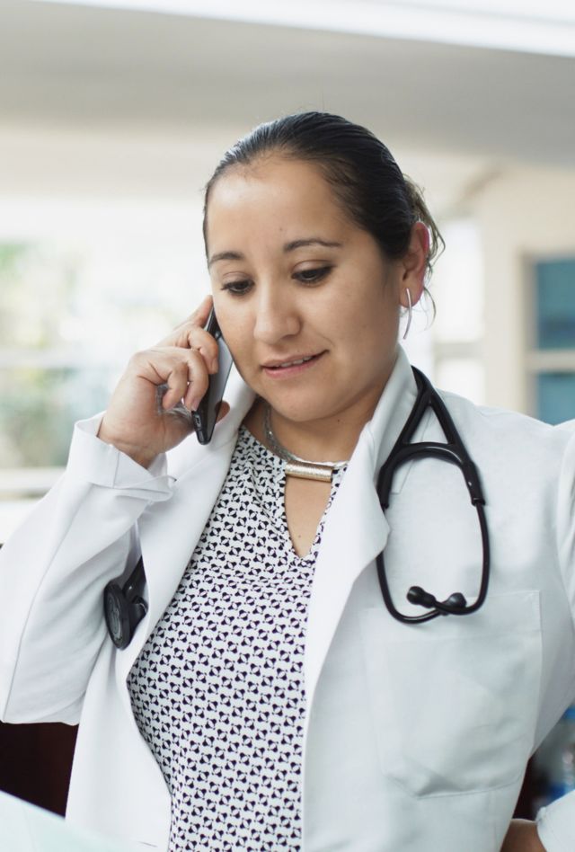 Hospital with medical doctor communicating on phone. Doctor's office with medical paperwork in the background. Doctor is in a hospital, healthcare professional on the cellphone