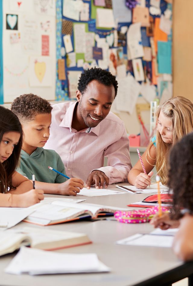 Male teacher works with elementary school kids at their desk