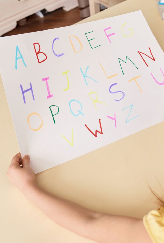 Tutor and student concept. Panoramic view of adult mother helping to her little daughter learning alphabet while they sitting behind desk, making home task for school together