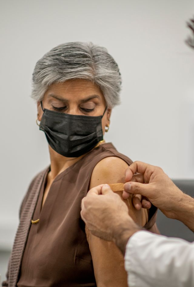 A male doctor puts a band aid on a senior woman's arm after he administered the COVID-19 vaccine injection. They are both wearing a protective face mask to protect themselves from the transfer of germs.