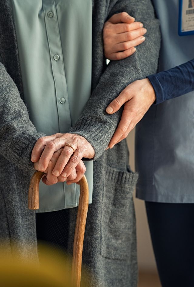 Close up hands of caregiver doctor helping old woman at private clinic. Close up of hands of nurse holding a senior patient with walking stick. Elder woman using walking cane at nursing home with nurse holding hand for support.