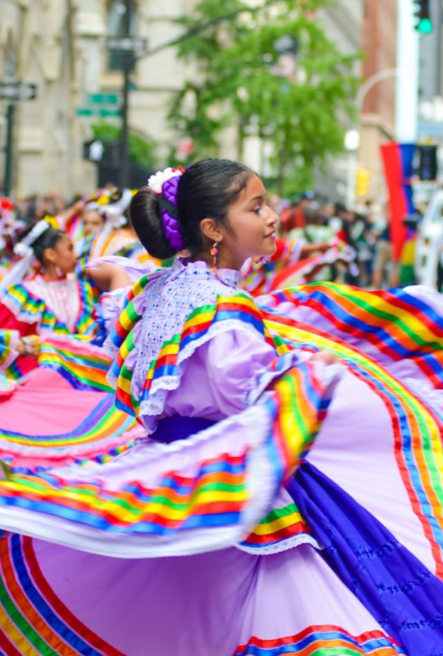 People wearing traditional folklorico clothing dancing in a street during a parade