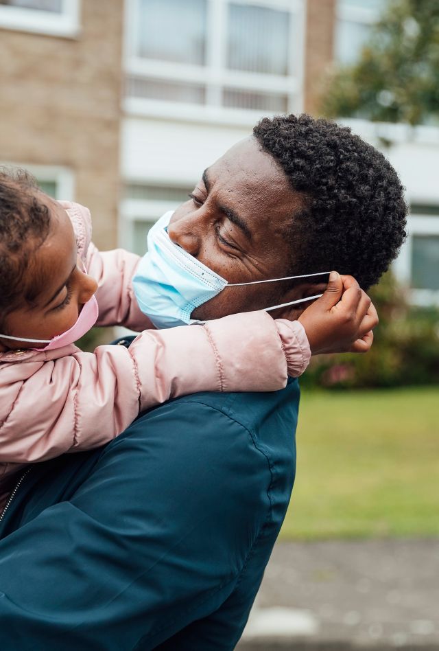 Close up of a young girl and her father wearing protective face masks during the Covid 19 pandemic outside. The girl is pulling her fathers mask.