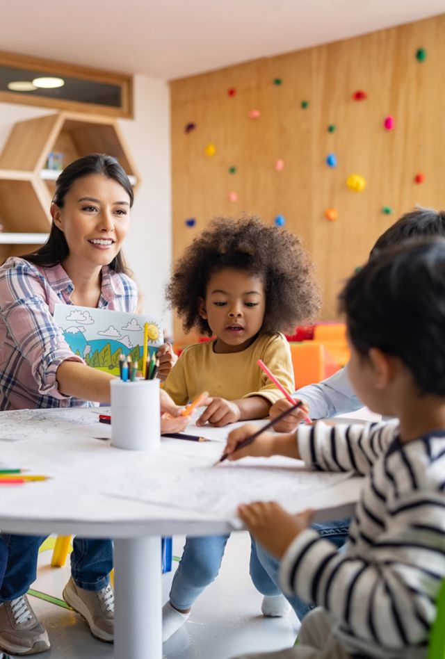 Happy group of Latin American children coloring in art class with the supervision of their teacher - elementary education concepts