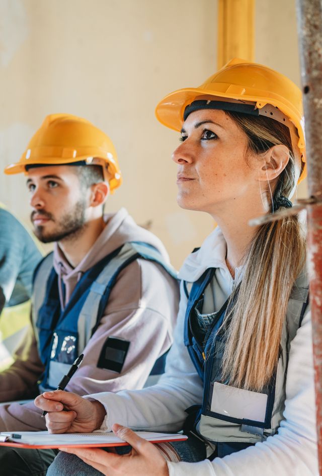 Young people wearing hard hats and taking notes on paper.