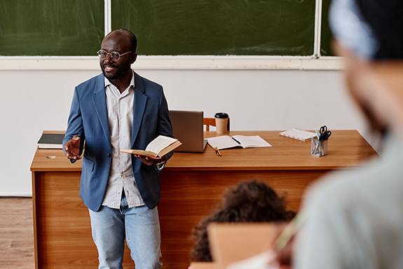 African teacher standing with book and reading lecture for students at university