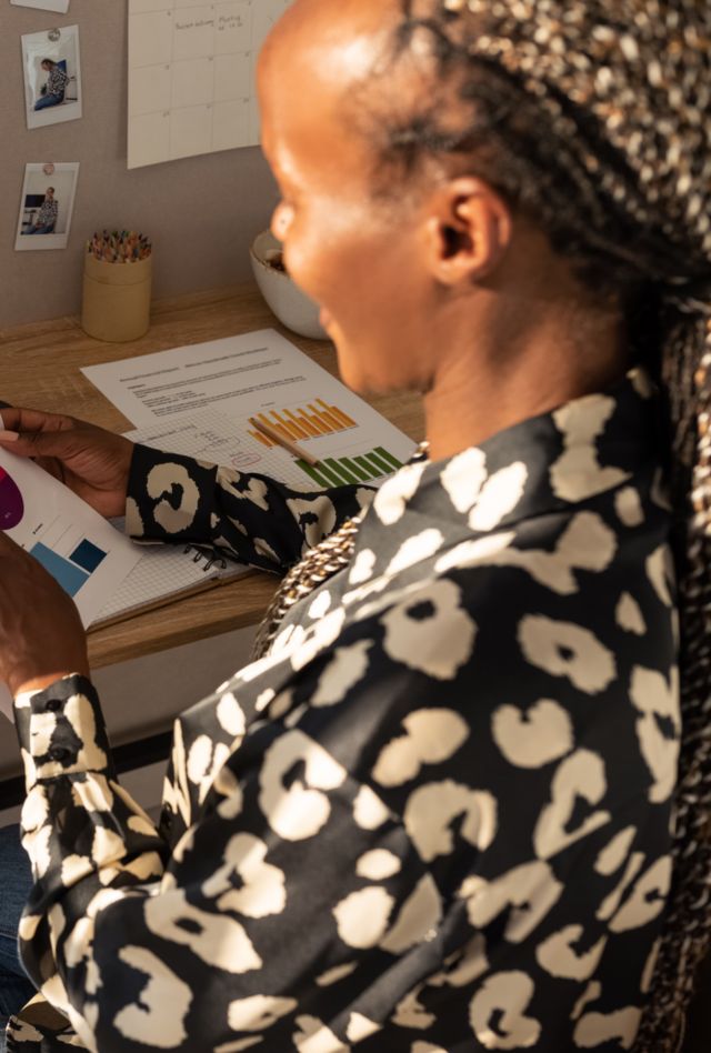 From above side view of crop positive African American female freelancer sitting at desk with documents and discussing project details with coworker during virtual meeting on sunny day