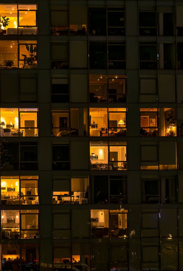 New York City - August 21, 2023: View of apartment windows at night as seen from the Brooklyn Bridge with lights from the bridge reflected on the outside of the apartment building in Brooklyn. From the Brooklyn Bridge walkway one can see directly into the illuminated apartments of this building on the Brooklyn side of the bridge at night.