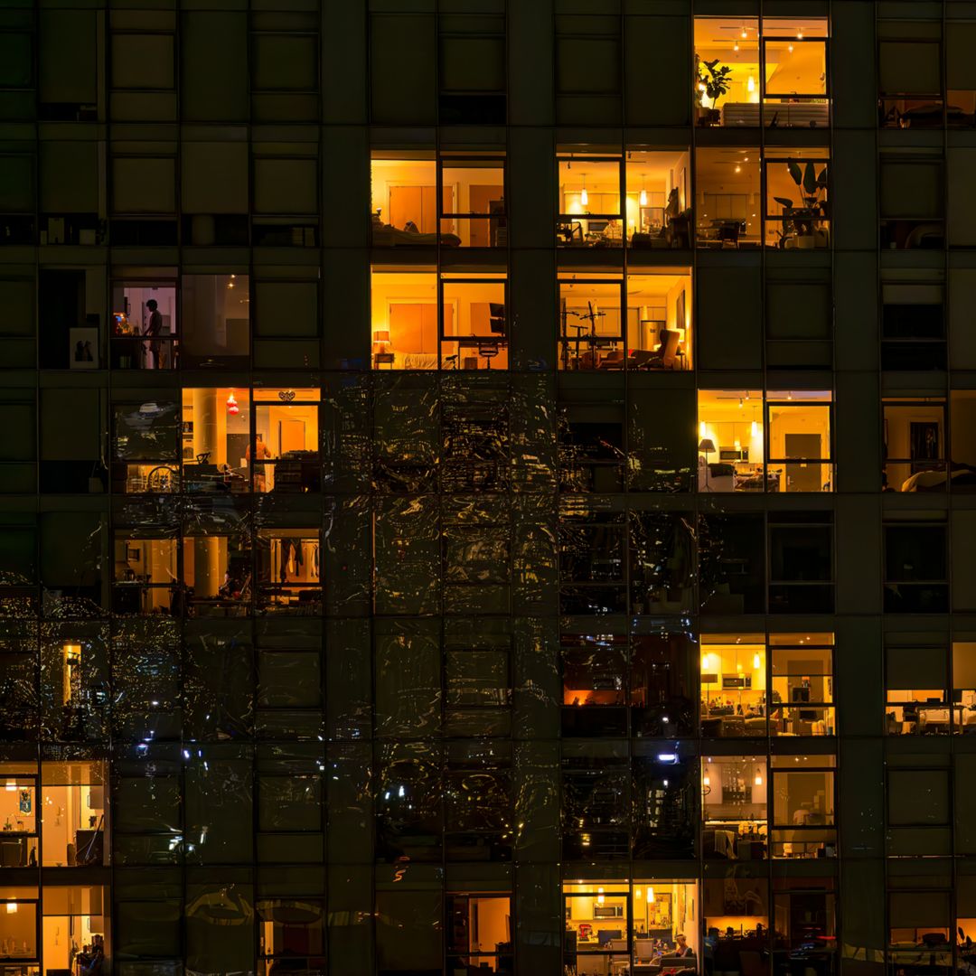 New York City - August 21, 2023: View of apartment windows at night as seen from the Brooklyn Bridge with lights from the bridge reflected on the outside of the apartment building in Brooklyn. From the Brooklyn Bridge walkway one can see directly into the illuminated apartments of this building on the Brooklyn side of the bridge at night.