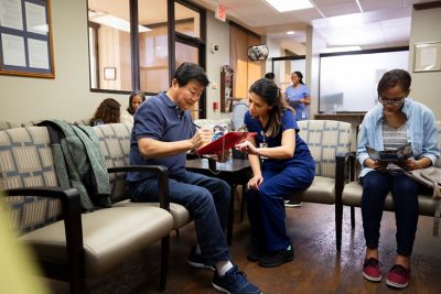 Mid adult nurse helps a senior man fill out a medical form as he waits to be seen by a doctor.