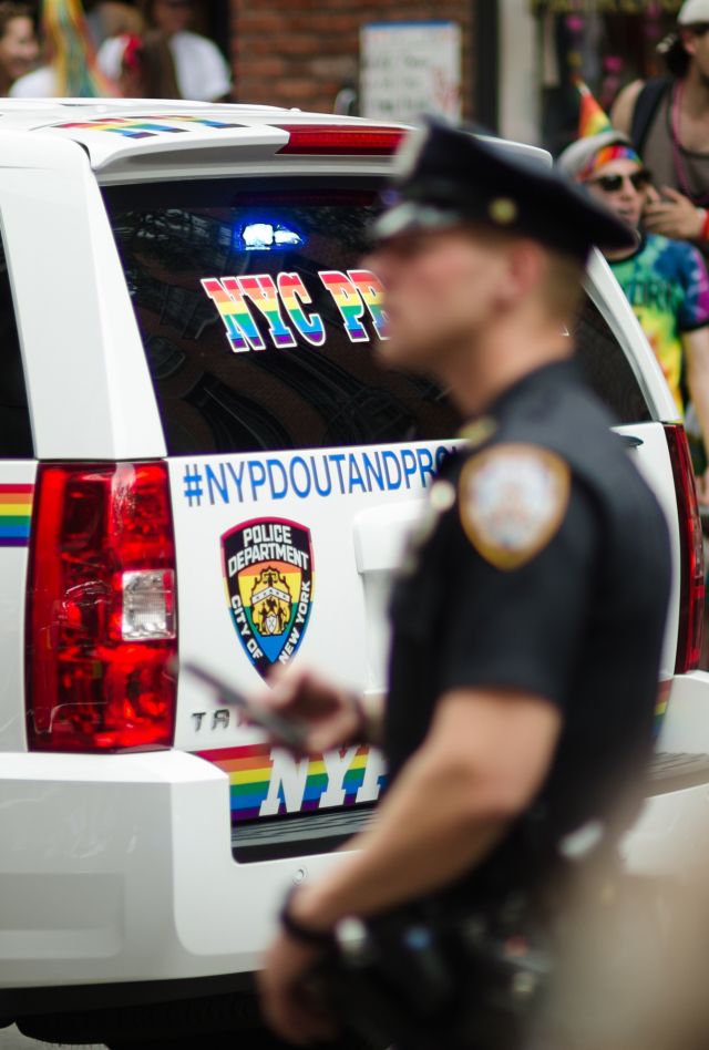 Policemen walk around a police car designed with rainbow decals on a New York City street during a pride parade.