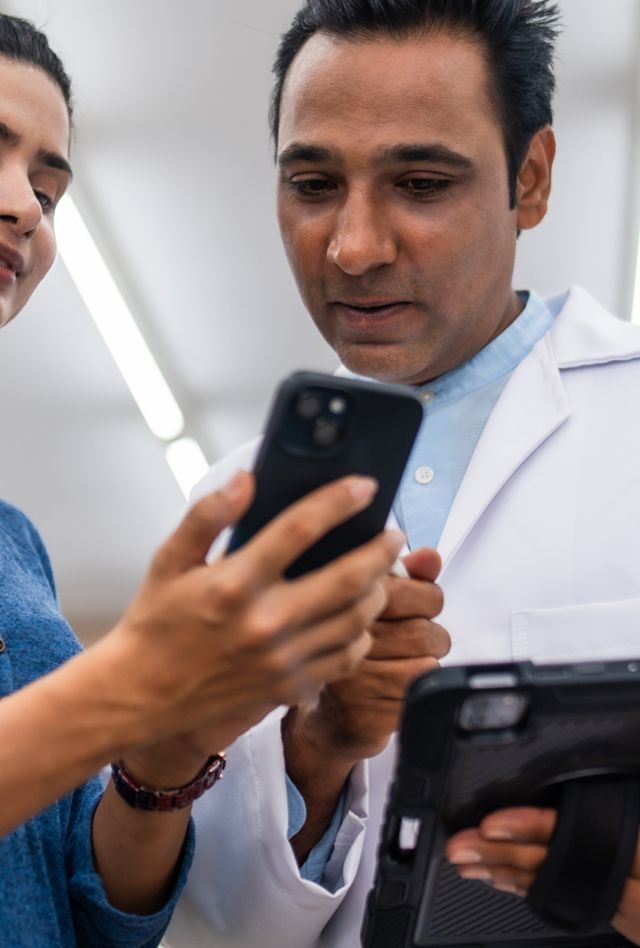 A pharmacist helps a customer using a digital tablet and smartphone in a modern pharmacy, discussing prescription medicine and healthcare options.
