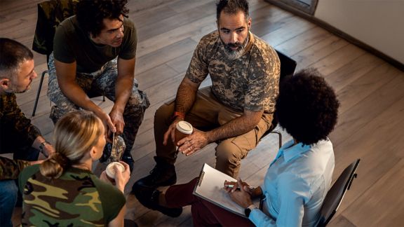 Group of diverse veterans talking during PTSD support group.
