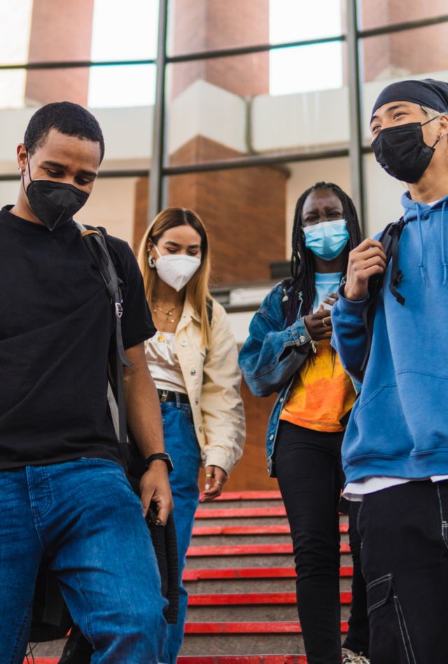 Low angle of company of multiracial friends wearing protective masks standing on stairs in city during coronavirus pandemic