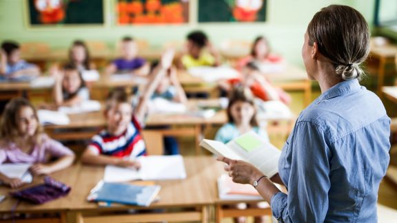 Back view of a female teacher teaching large group of elementary students in the classroom.