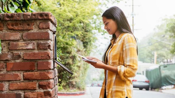 Woman in a yellow shirt standing in front of a mailbox looking at her mail