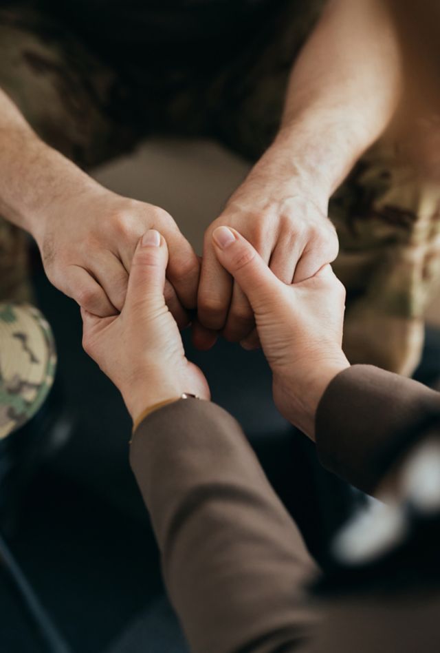 Close-up of man in military fatigues holding both hands with woman as though receiving support and encouragement.
