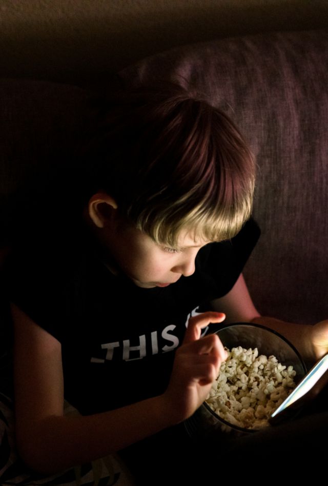 9 years old kid with a bowl of popcorn watching a movie on a smartphone