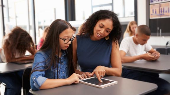 Teacher helping teenage schoolgirl with tablet computer