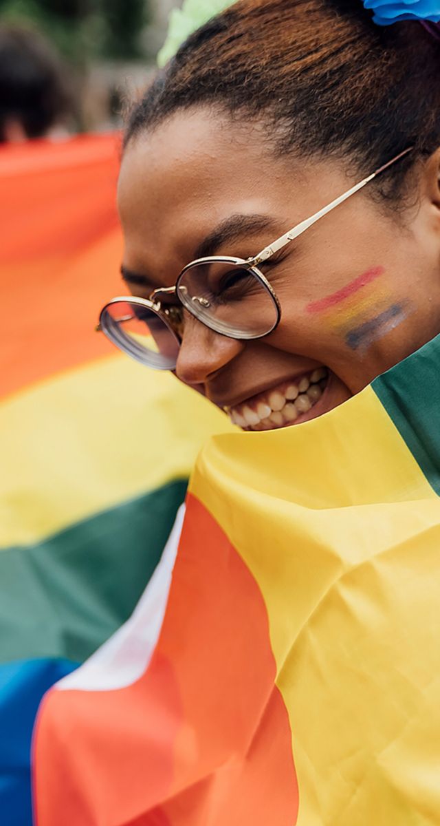 Smiling female with rainbow face paint, wrapped in a rainbow flag