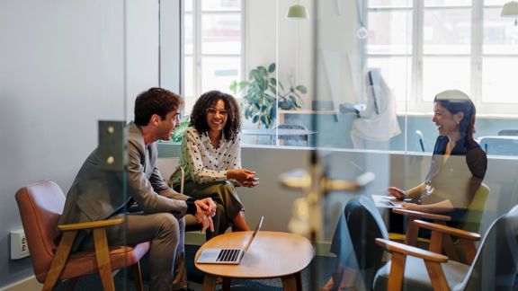 Three coworkers around a small table in a meeting room