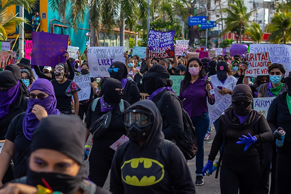 Crowd of people in the street holding protest signs in Spanish and wearing masks and head scarves.