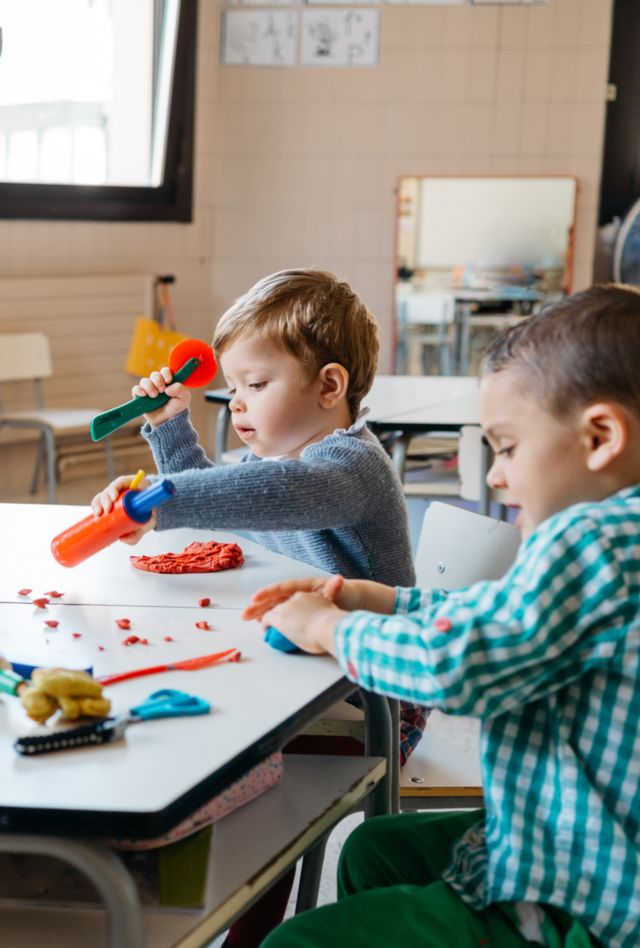 Group of toddlers sitting at table and playing with soft modelling clay in a classroom