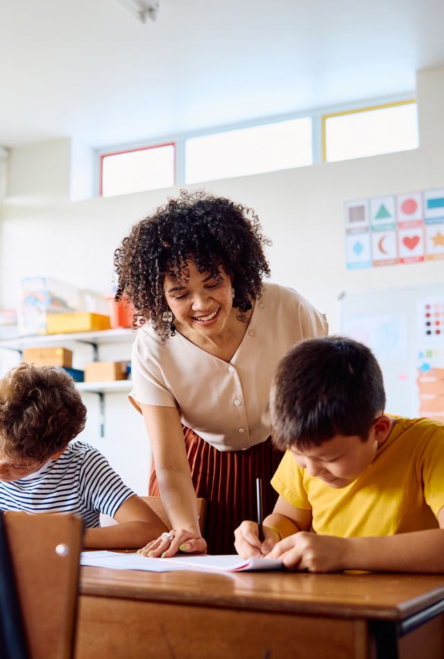 School teacher helping male student sitting at desk with happy expression