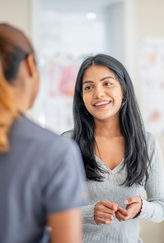 A young female adult of Asian descent is smiling at her female nurse. She is at a doctor's office for a medical check up.