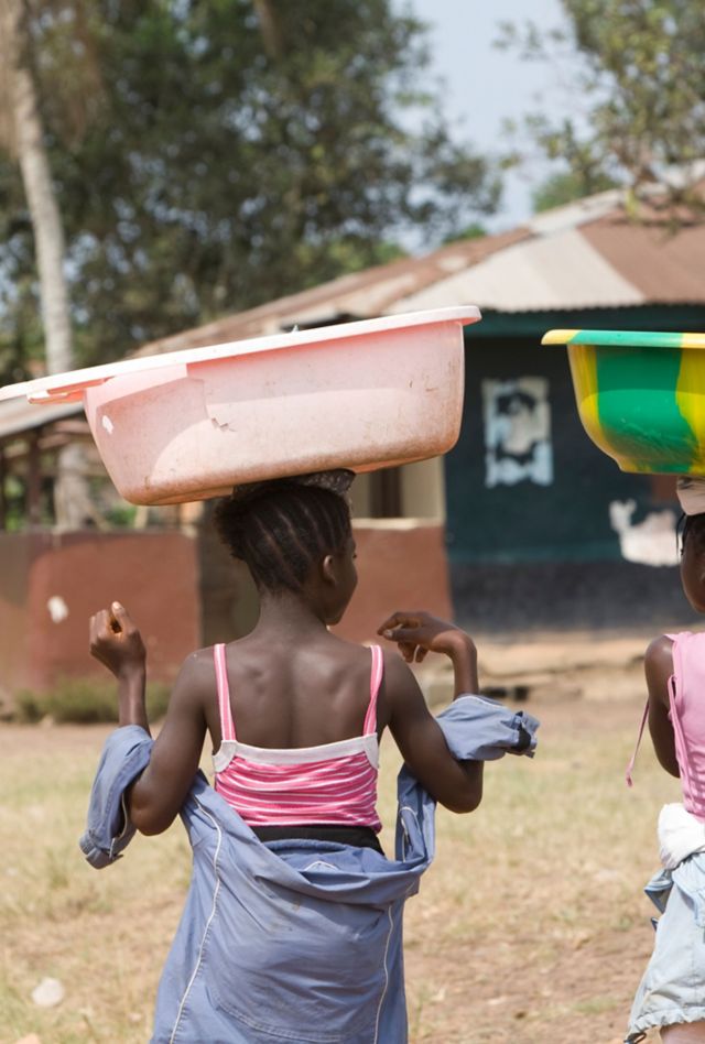 BX6508 Girls with buckets balanced on their heads walk along the main street in Kakata, Liberia, West Africa.