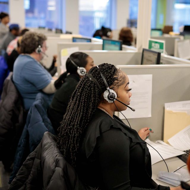 Woman sitting at a desk working on a laptop while talking on a headset