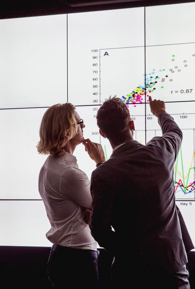 Two people in a dark room standing in front of a large data display