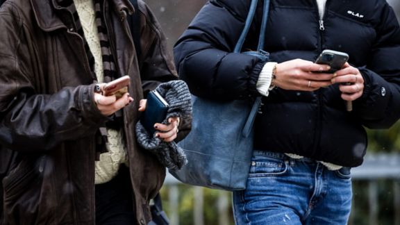 Close up of two people walking side by side as they text