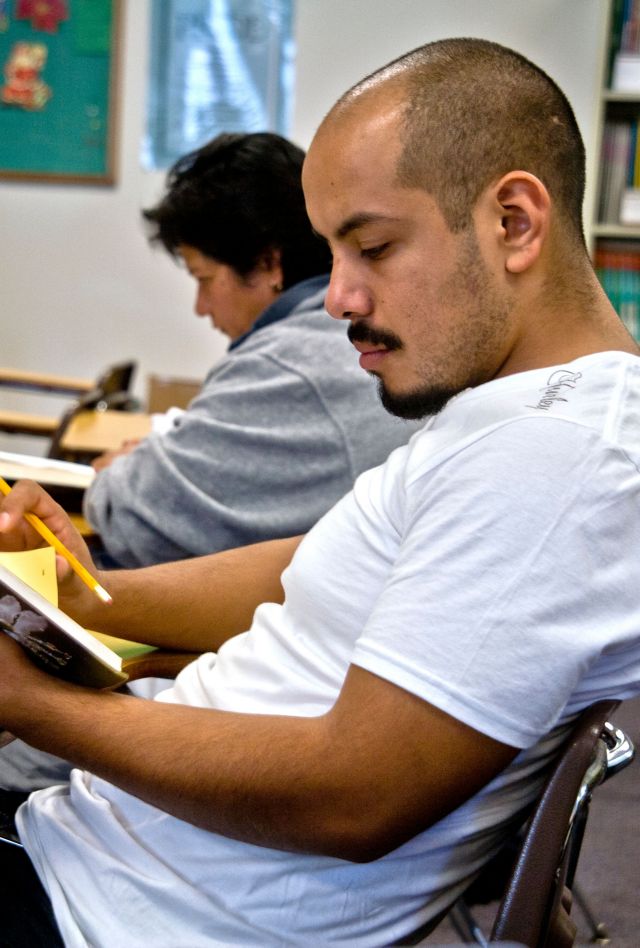 BX5AMC A Hispanic young adult studies a grammar textbook in a community adult basic literacy class in San Juan Capistrano, California.