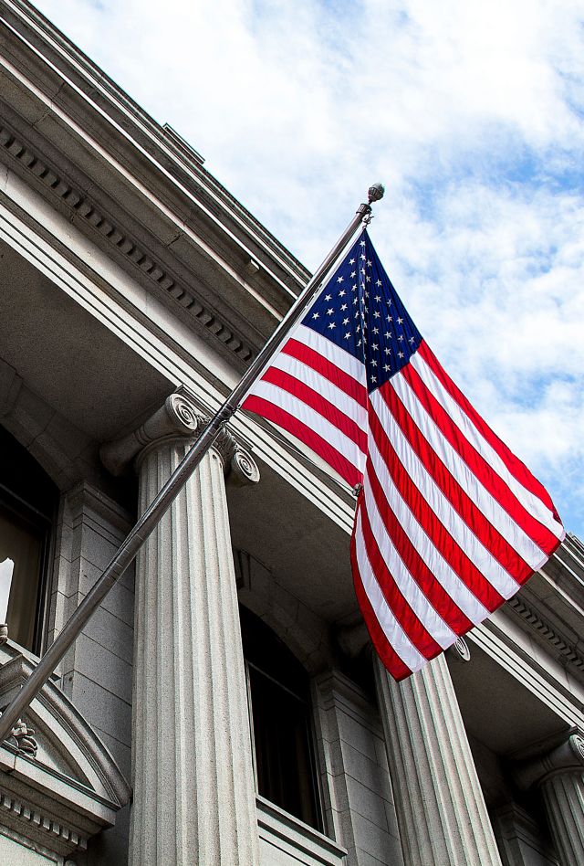 Stone granite official government building in city with American flag waving in front