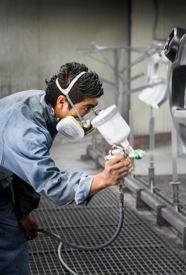 Worker wearing protective mask spray painting a piece of a product.