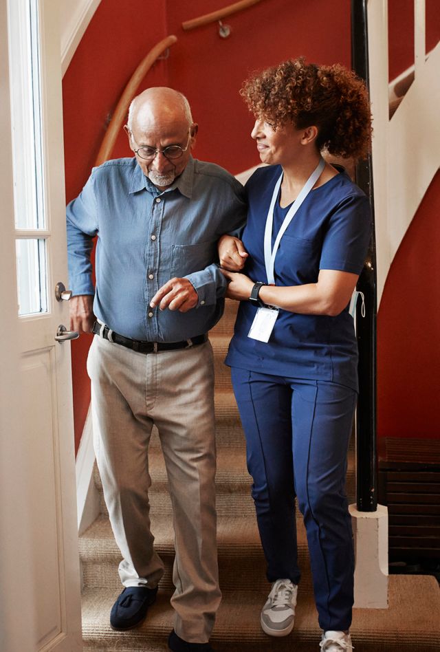 Mature female nurse walking with senior man on steps at home