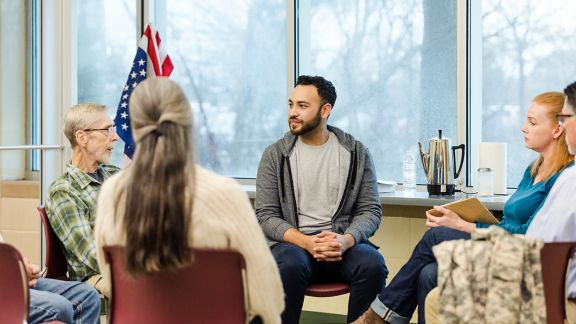 A multiracial, multigenerational group of military vets meet for group therapy on the Air Force base.