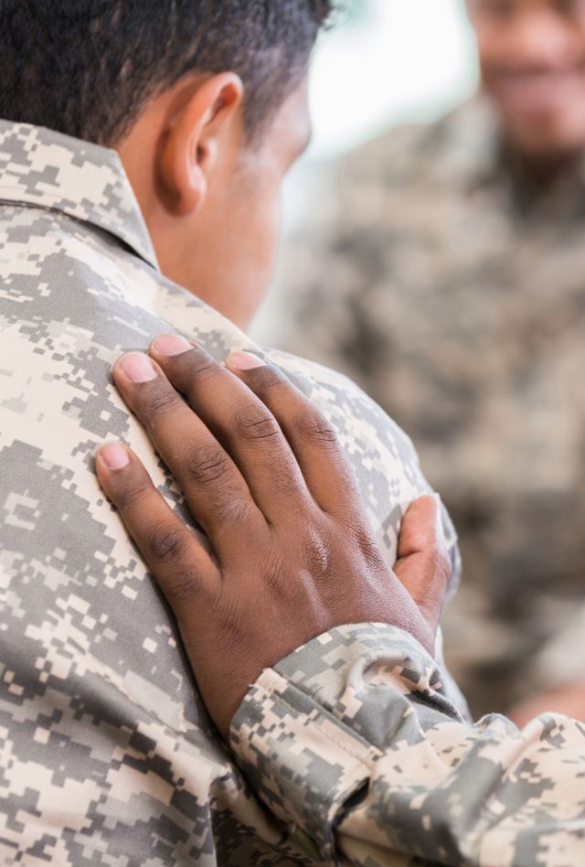 Unrecognizable soldier places his hand on fellow soldier while praying for him during a support group meeting