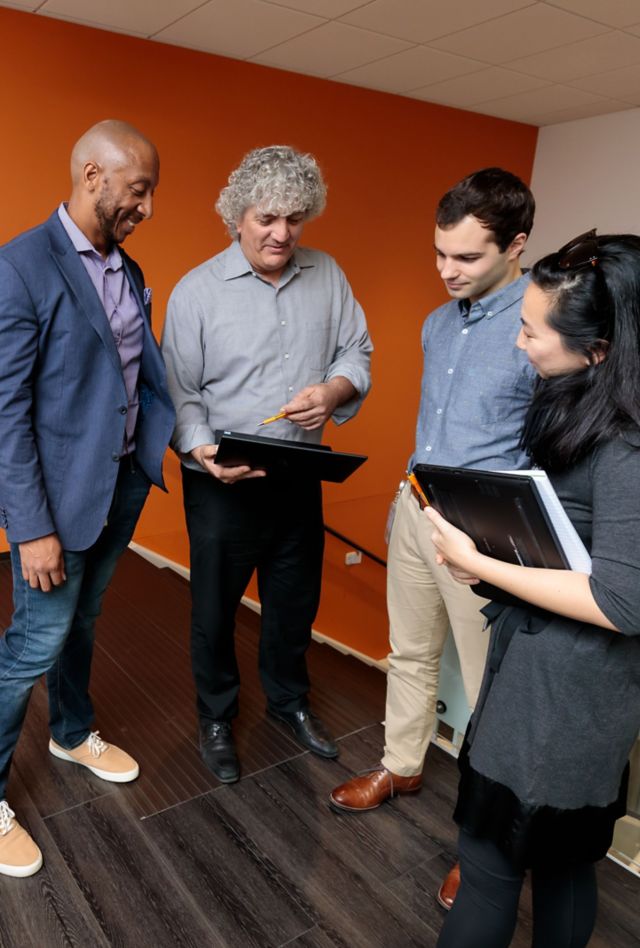 Three people smiling and talking at conference table while working on laptop computers