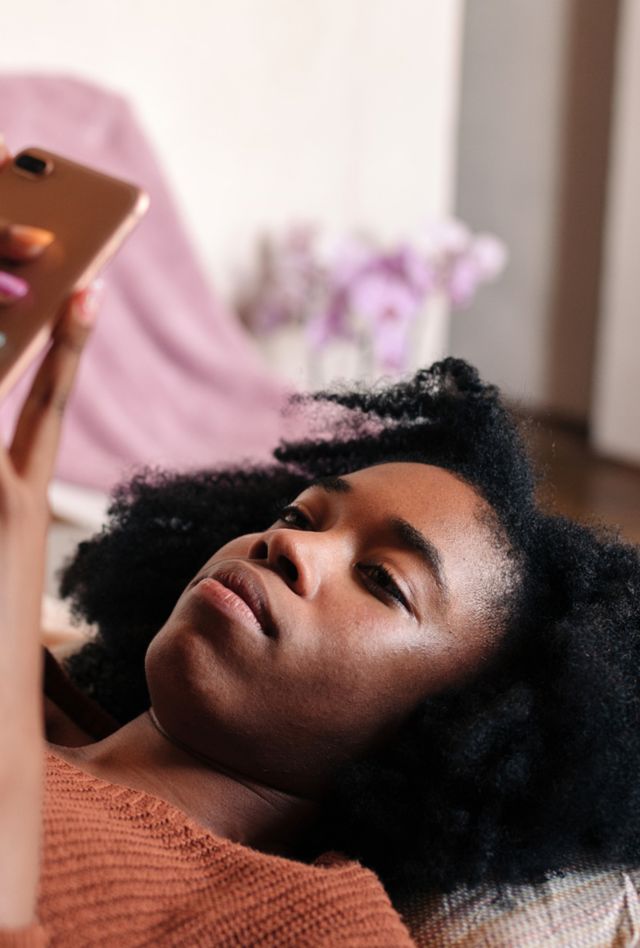 Young woman lying in bed looking at her smartphone.